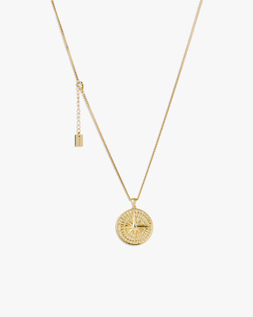 Gold compass necklace with a round pendant on a light grey background