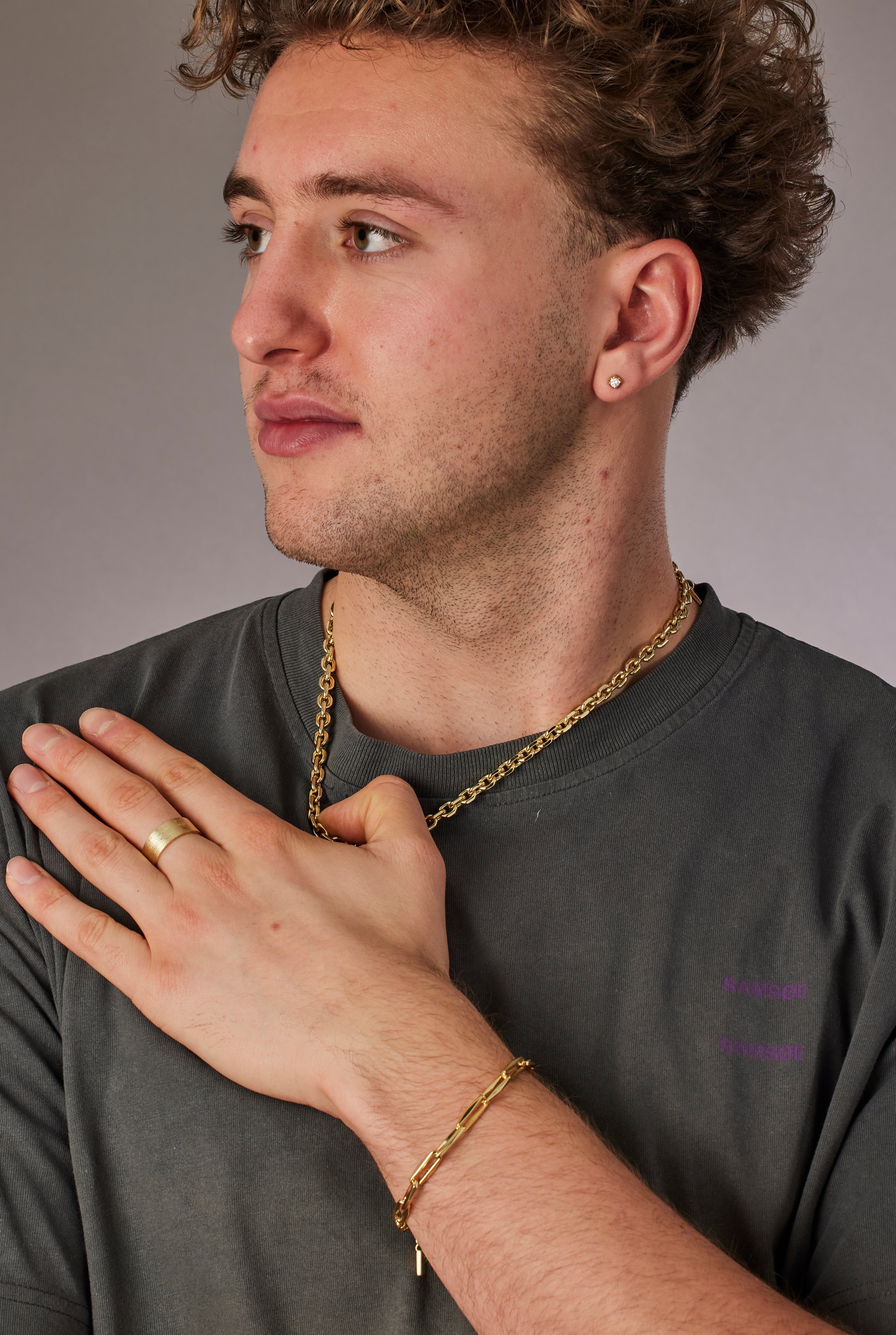 Man wearing a gold chain and ring, with another hand touching his chest against a neutral background