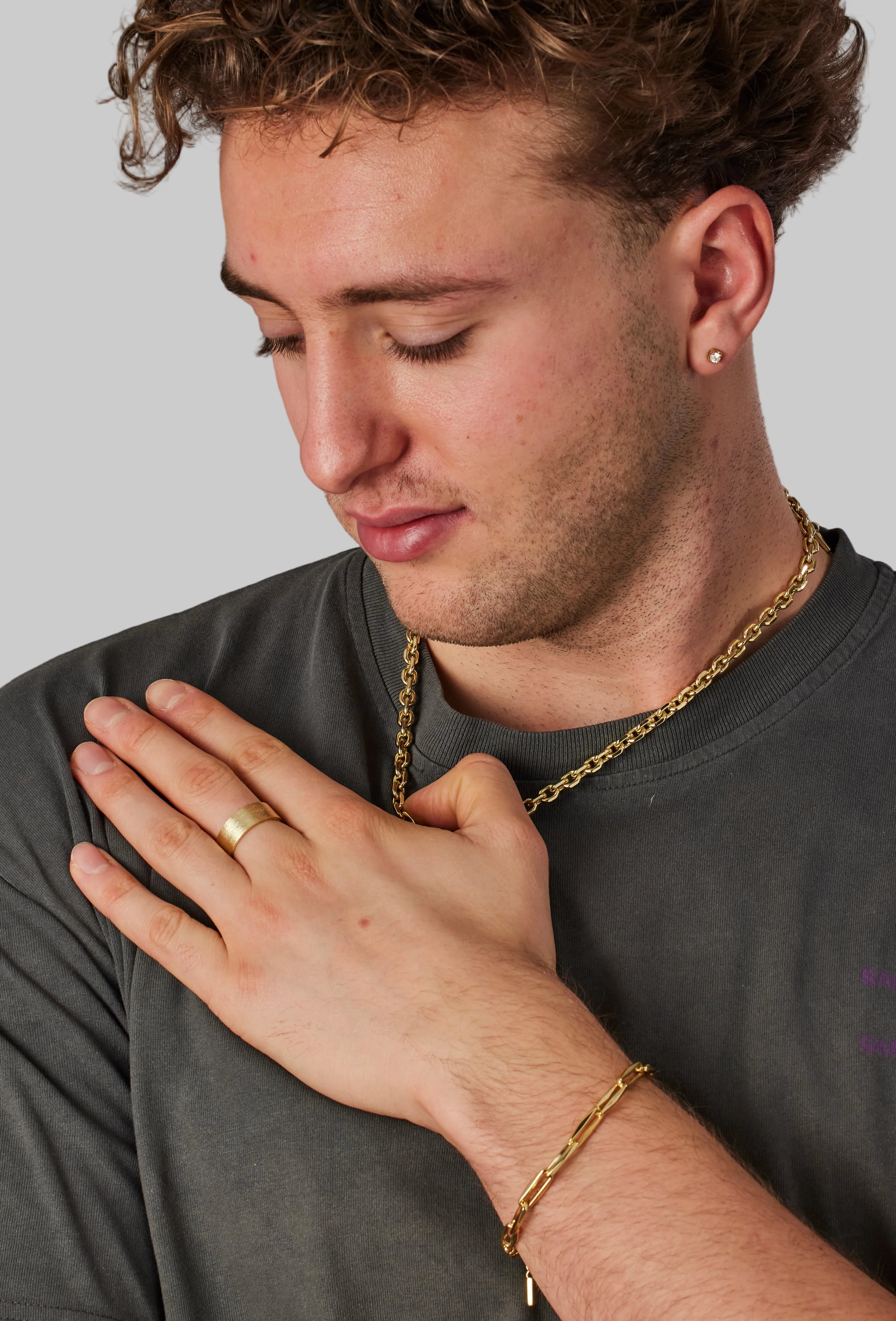 Man wearing gold jewelry including a ring, bracelet, and necklace against a neutral background