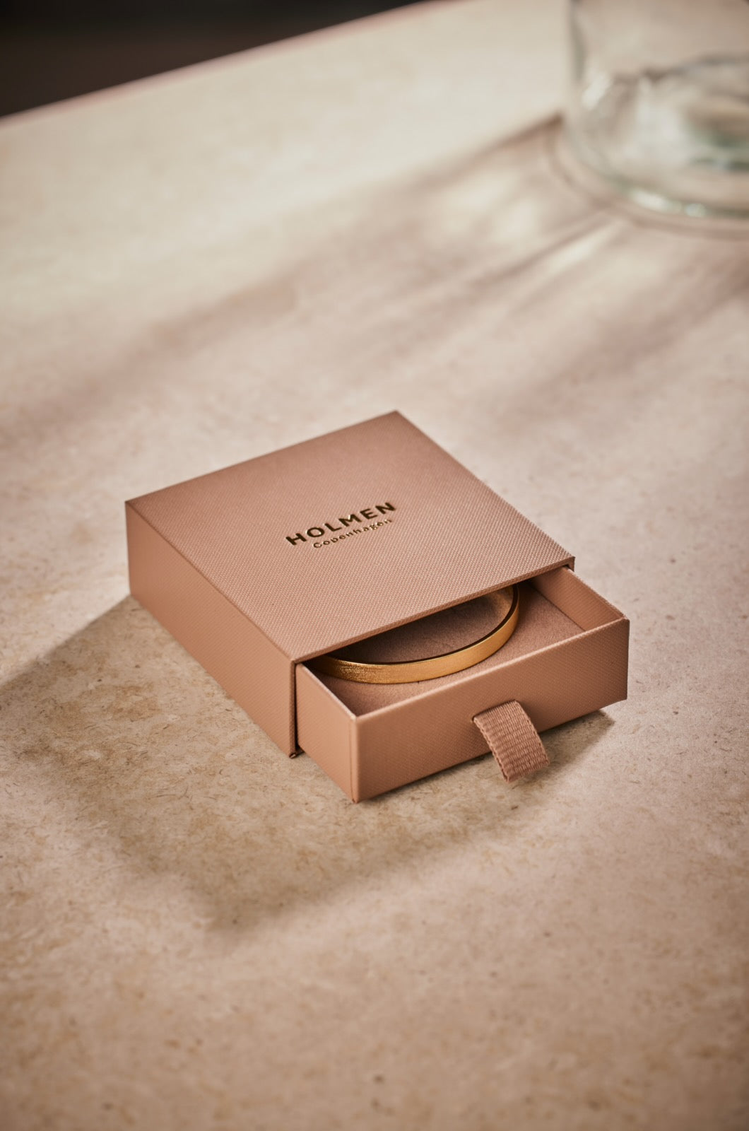 Brown packaging box with 'HOLMEN' branding on a beige surface