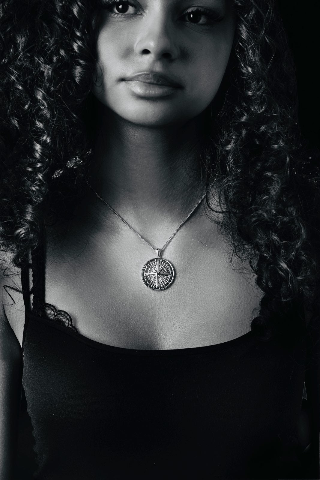 Black and white portrait of a woman wearing a necklace with a circular pendant.