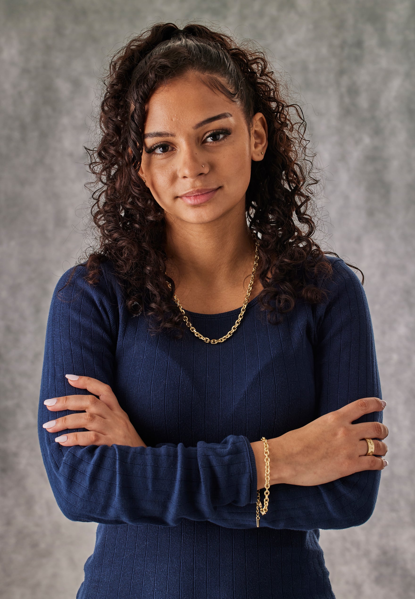 Woman wearing a blue top with gold jewelry against a gray background