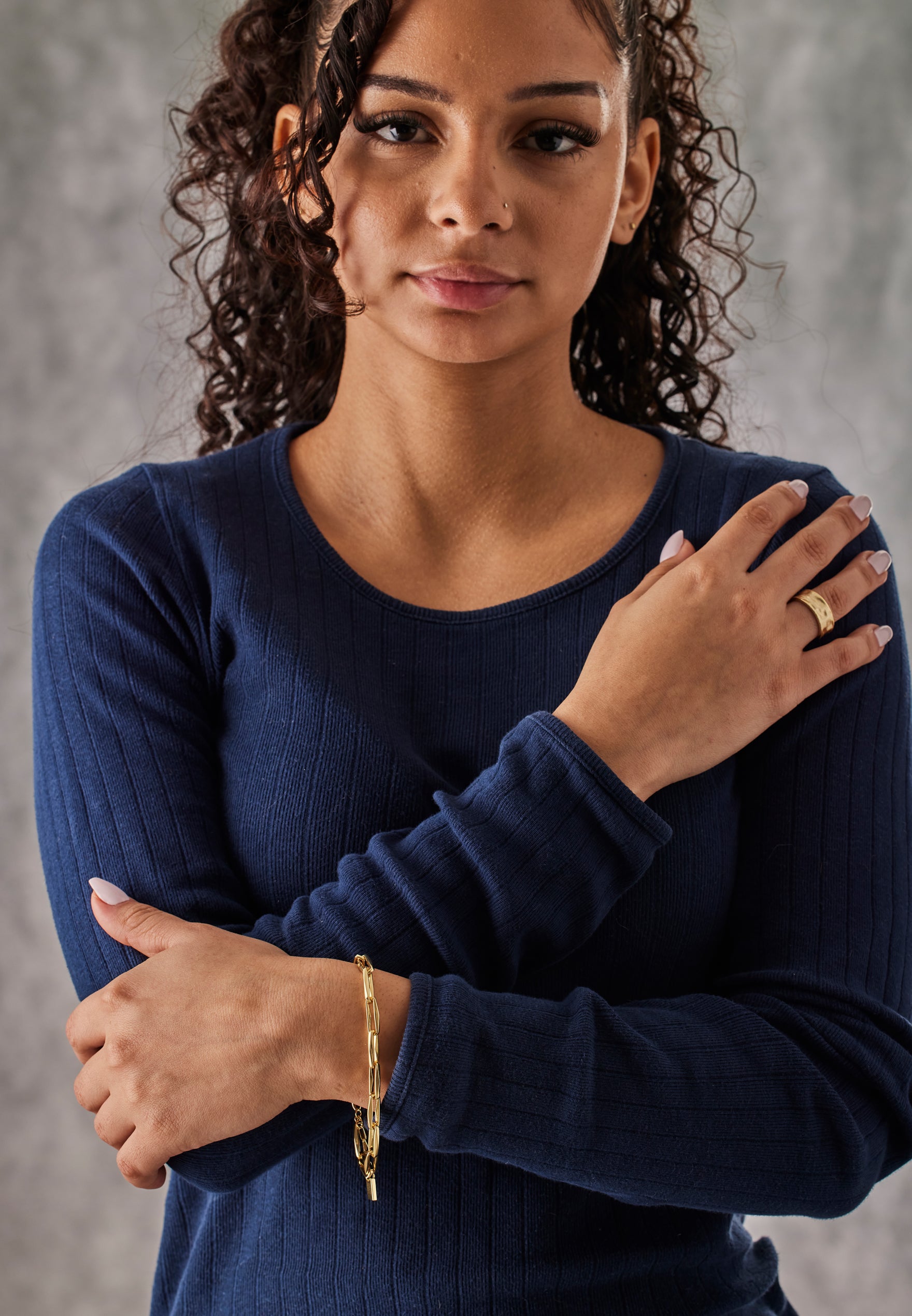 Woman wearing a navy blue sweater with a gold bracelet against a gray background