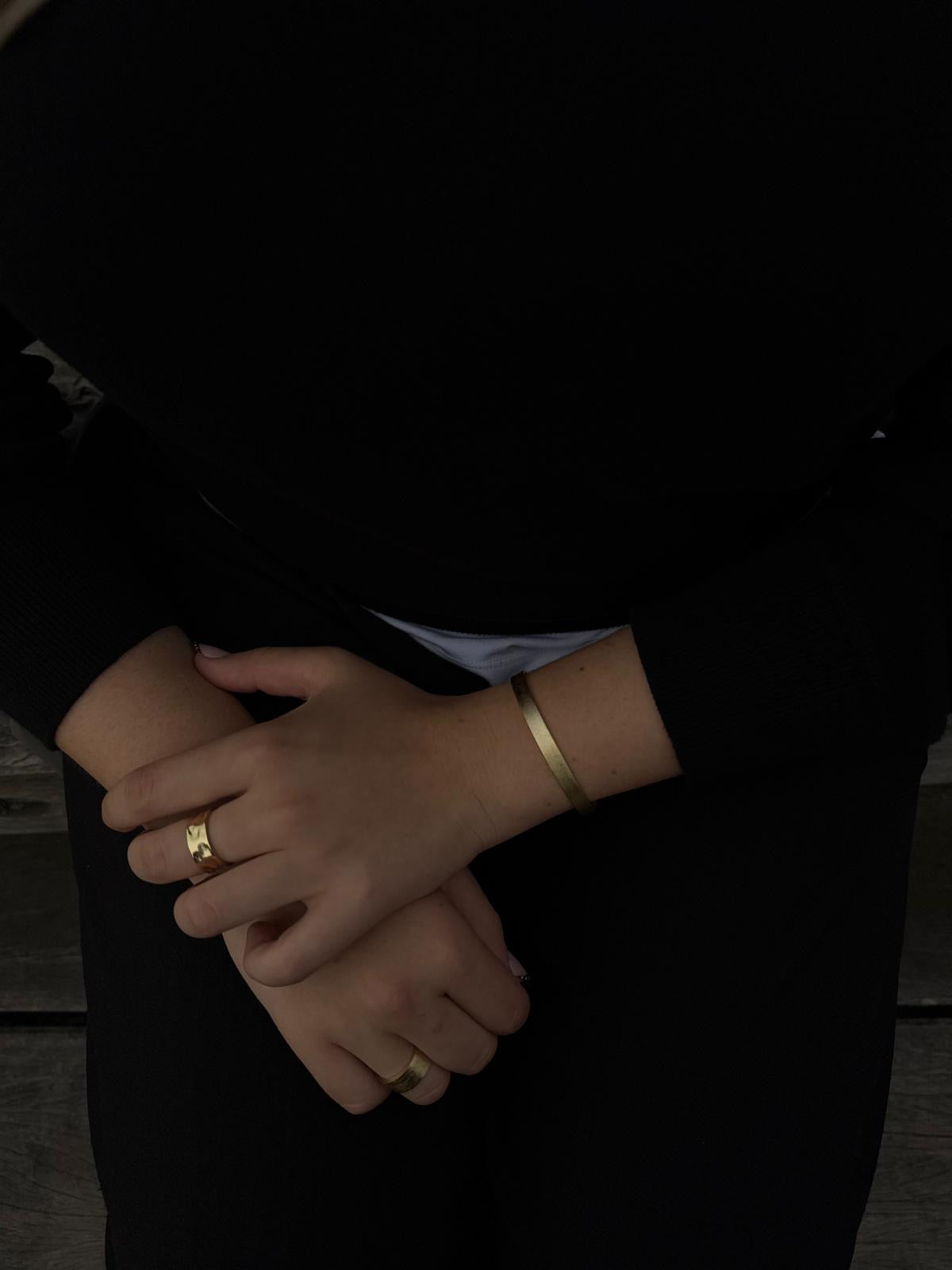 Close-up of hands with gold rings and bracelet on a dark background