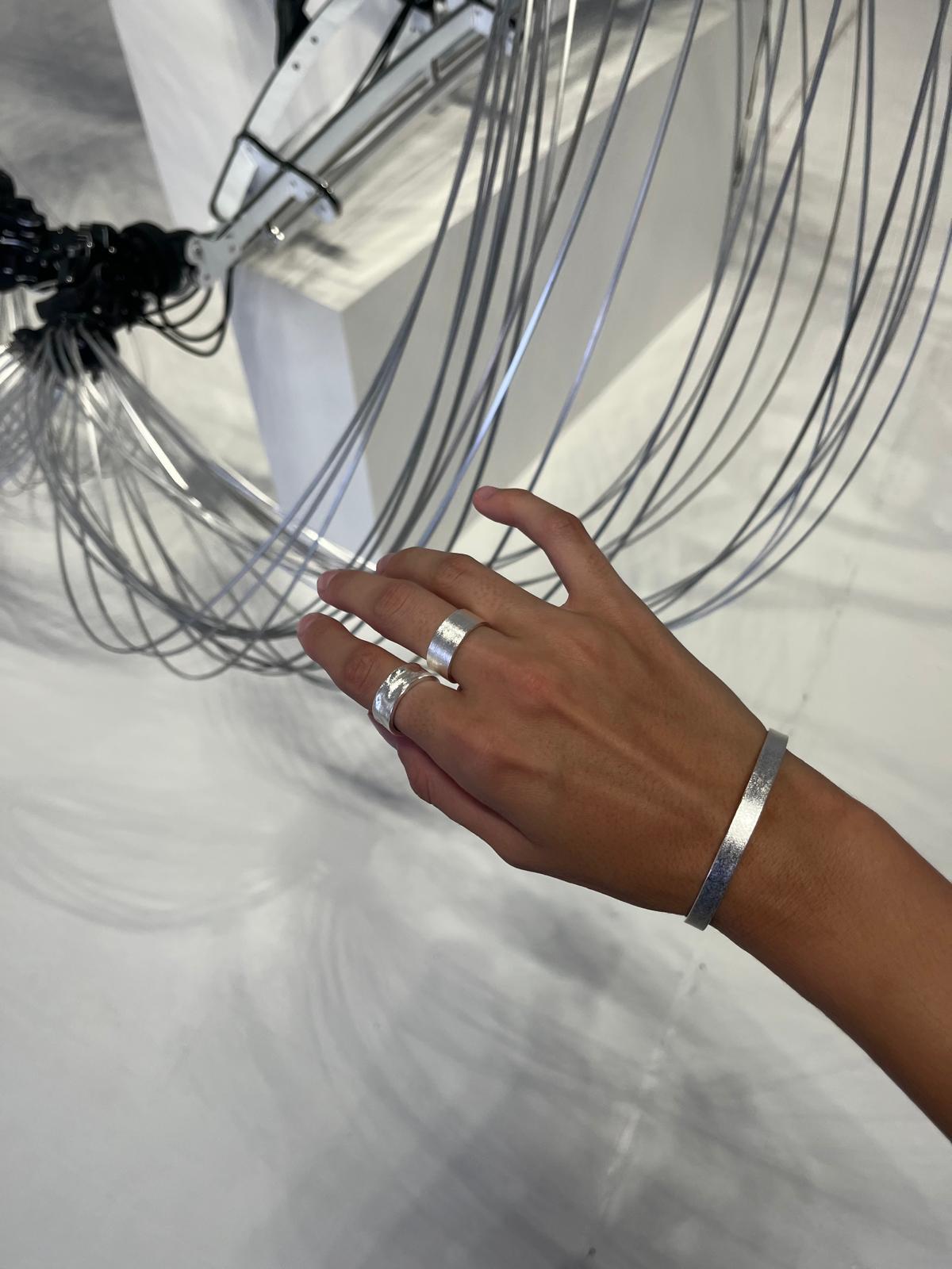 Hand with silver rings and bracelet holding a coiled wire against a white background