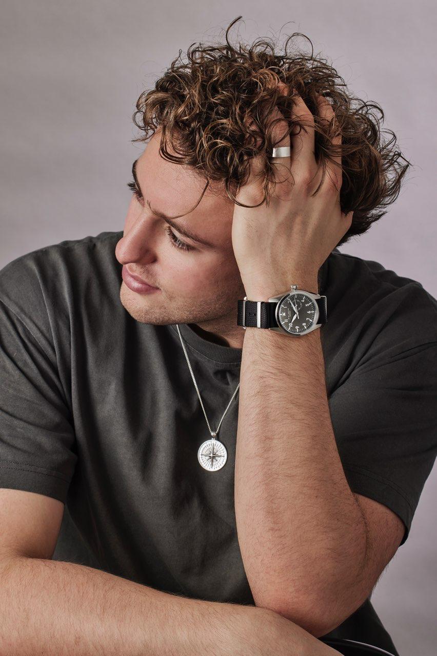 Man wearing a black shirt and a watch, with a neutral background
