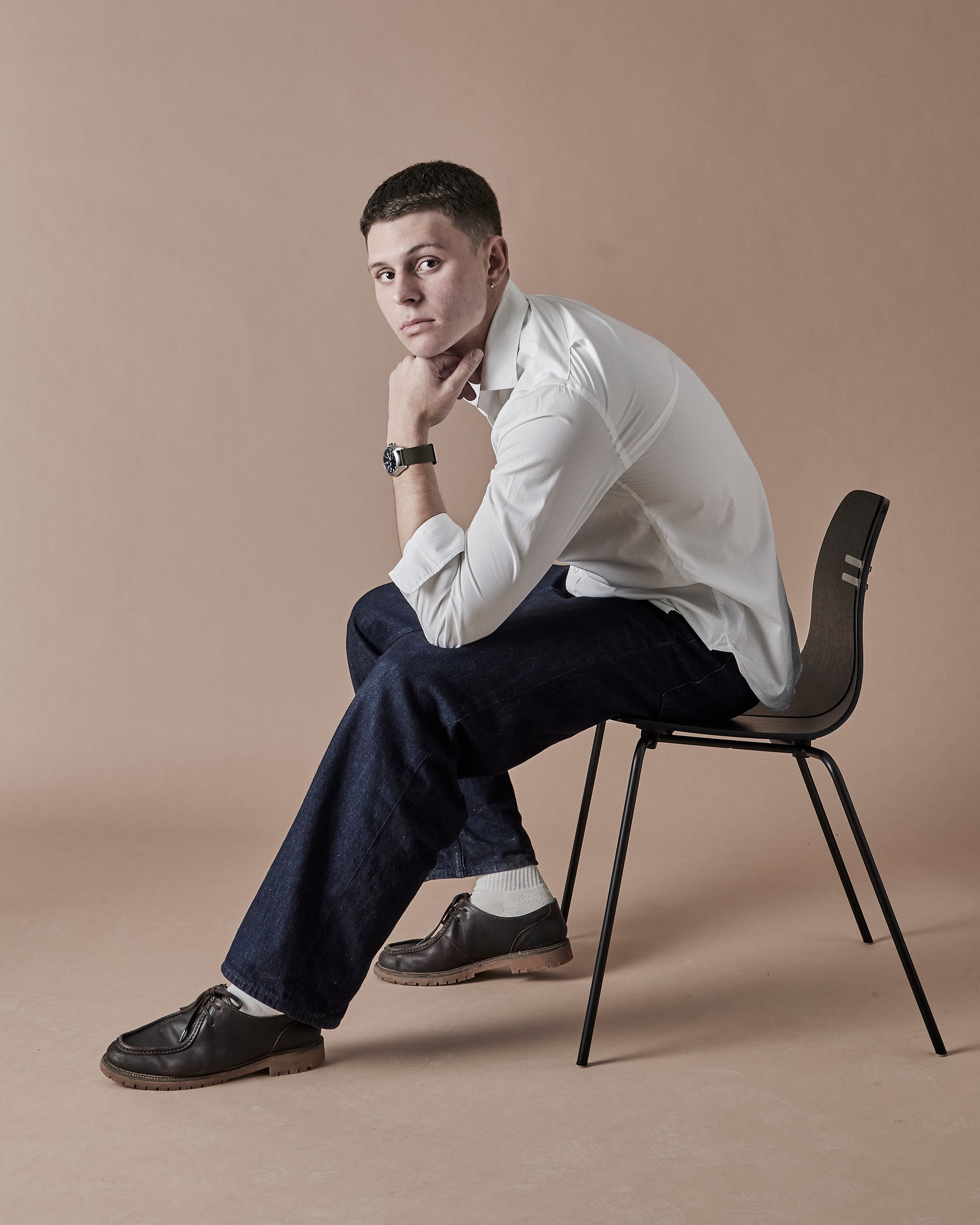 Man sitting on a chair wearing a white shirt and dark pants against a beige background