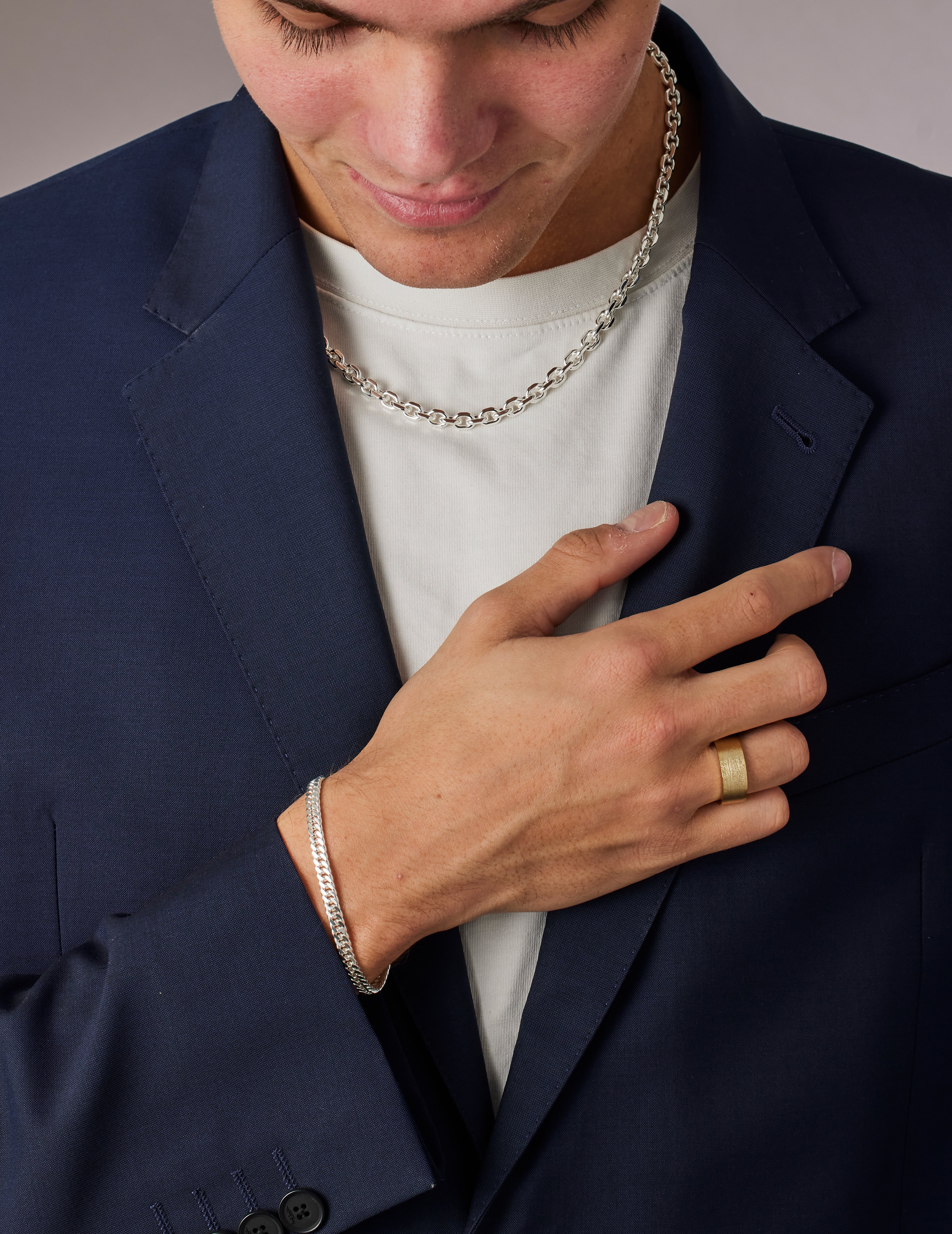 Man wearing a navy blazer, white shirt, and gold ring with a neutral background