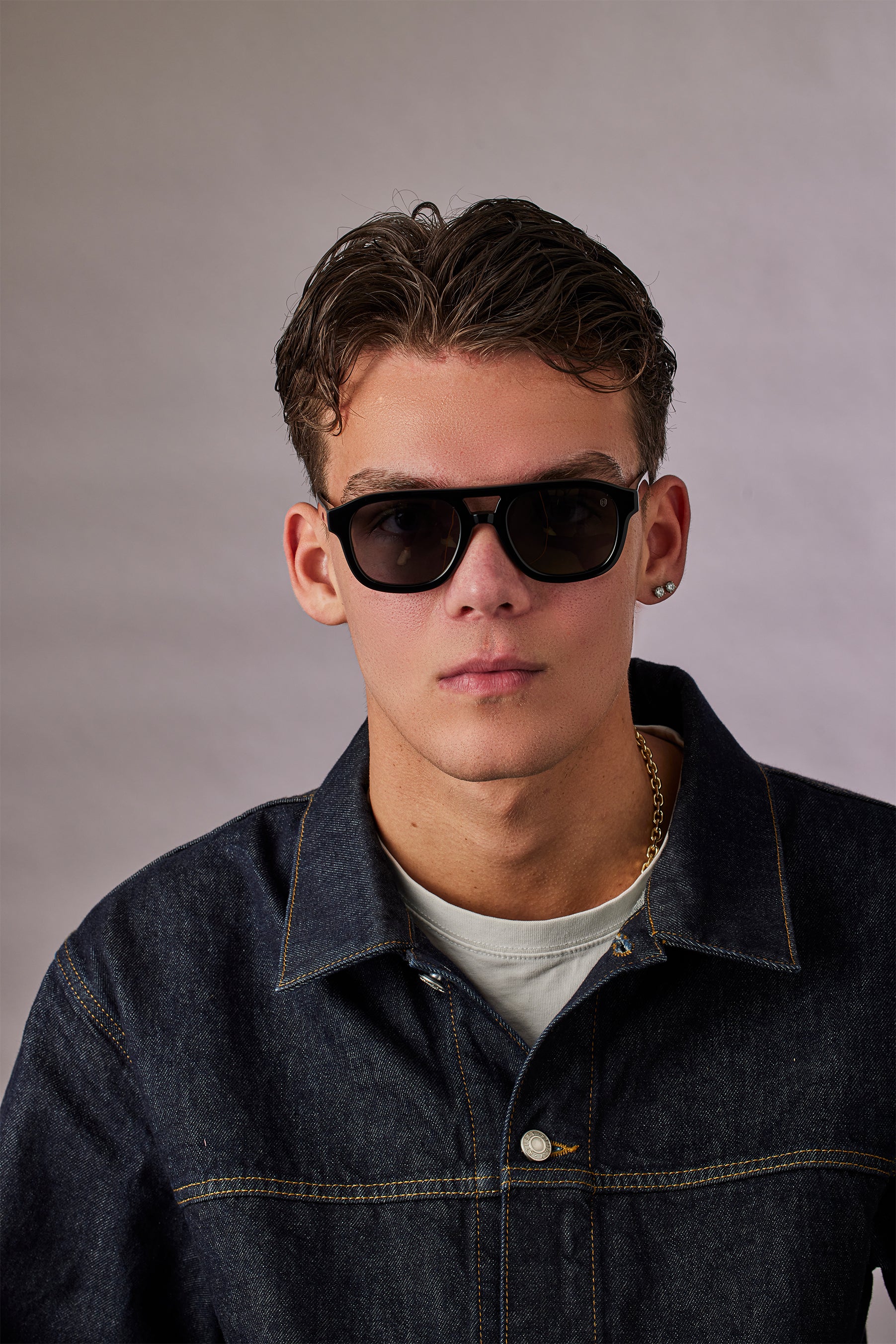 Man wearing sunglasses and a denim jacket against a plain background
