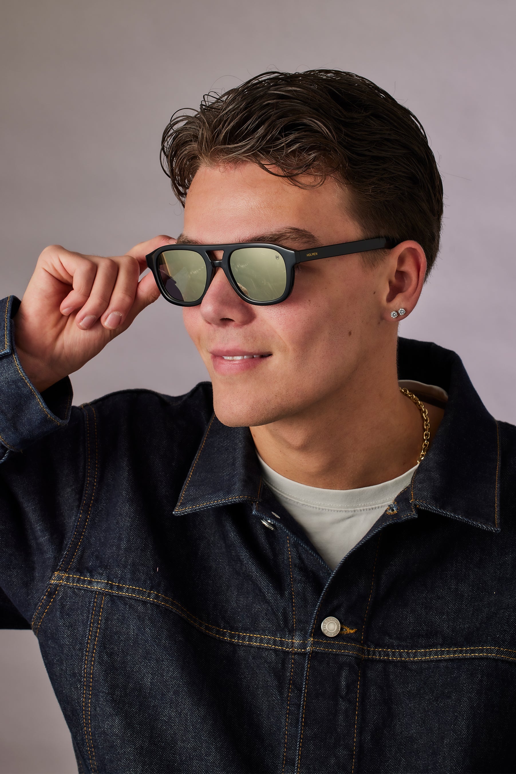 Man wearing sunglasses and a denim jacket against a neutral background