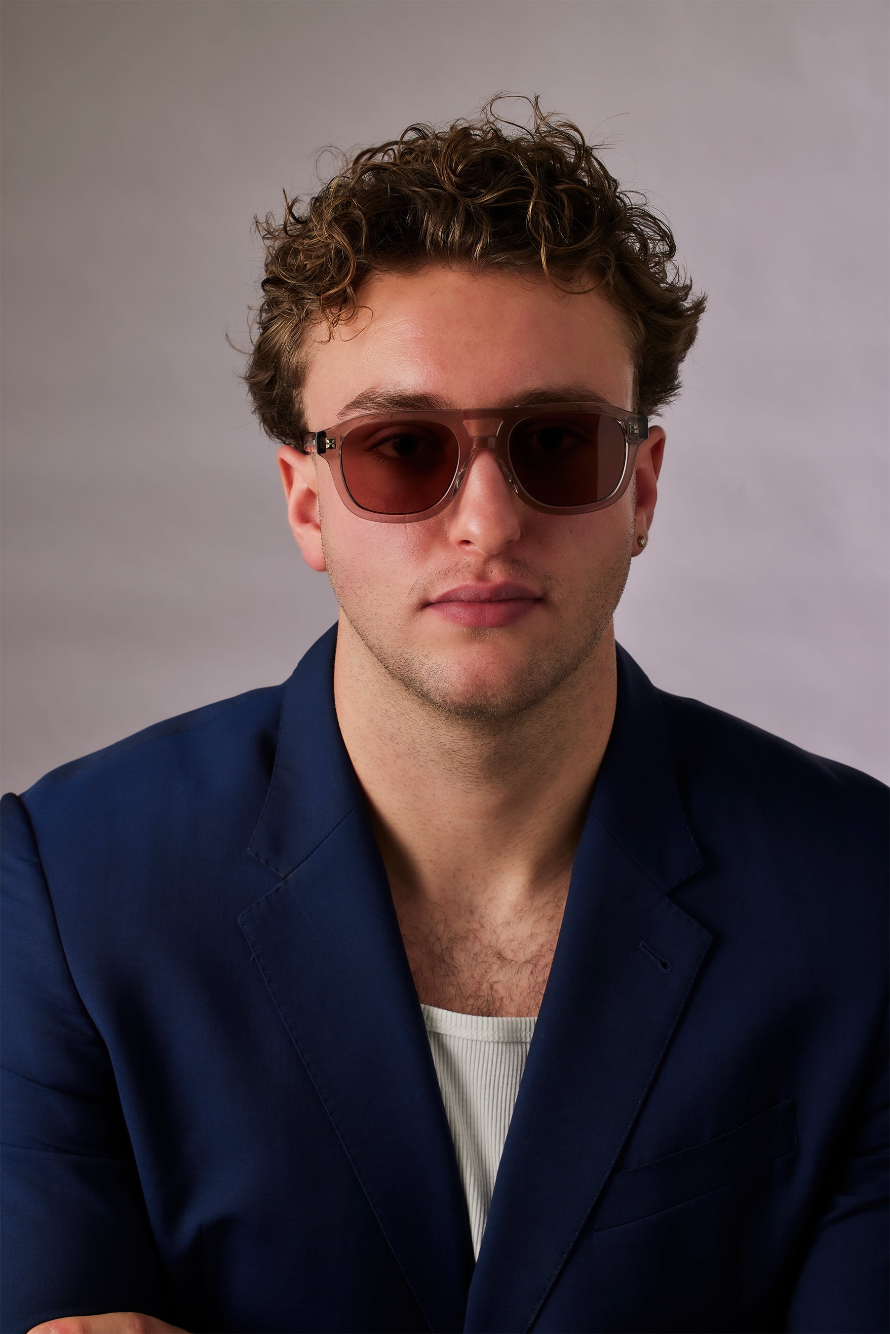 Man wearing sunglasses and a blue blazer against a plain background