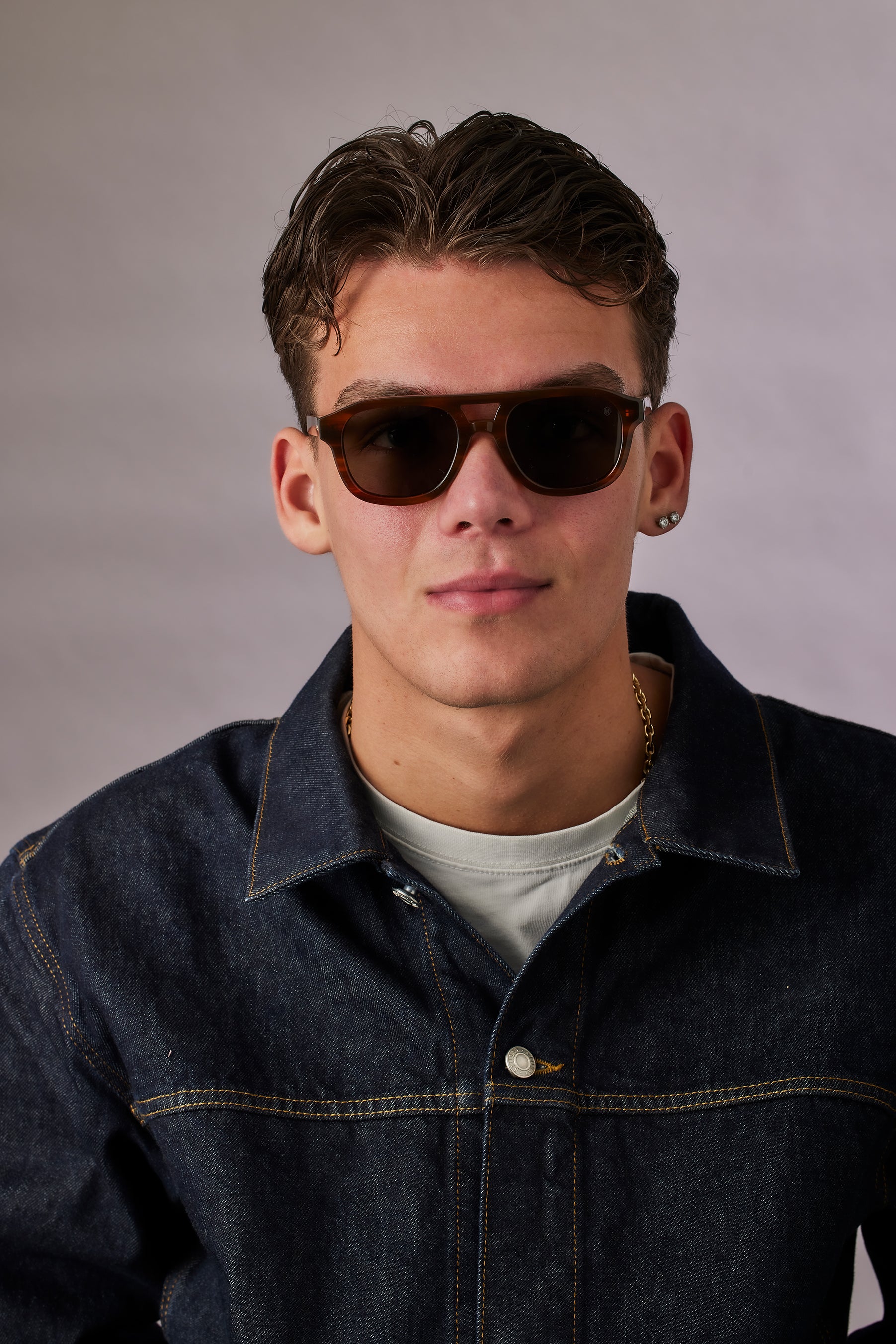 Man wearing sunglasses and a denim jacket against a plain background