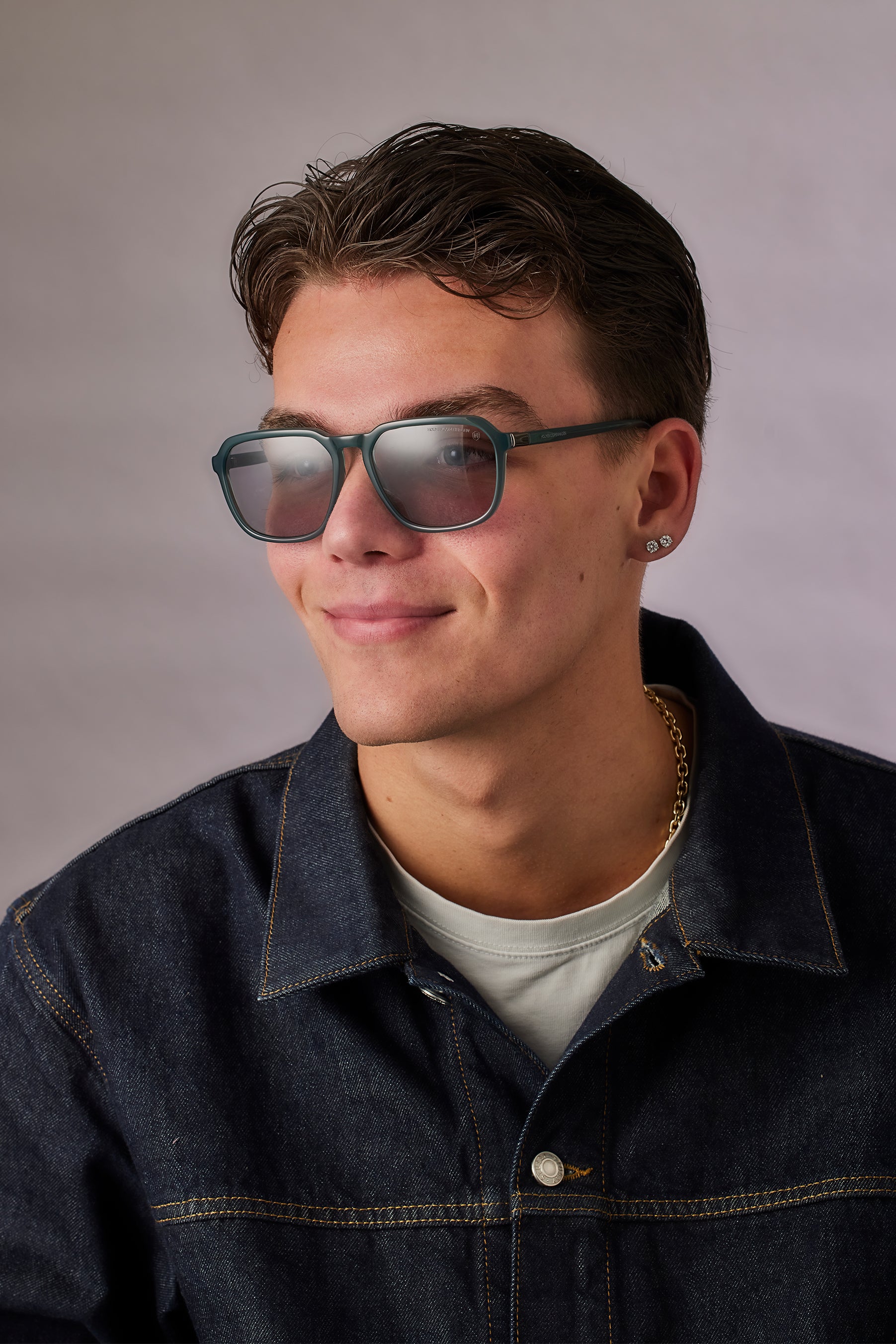 Man wearing sunglasses and a denim jacket against a plain background
