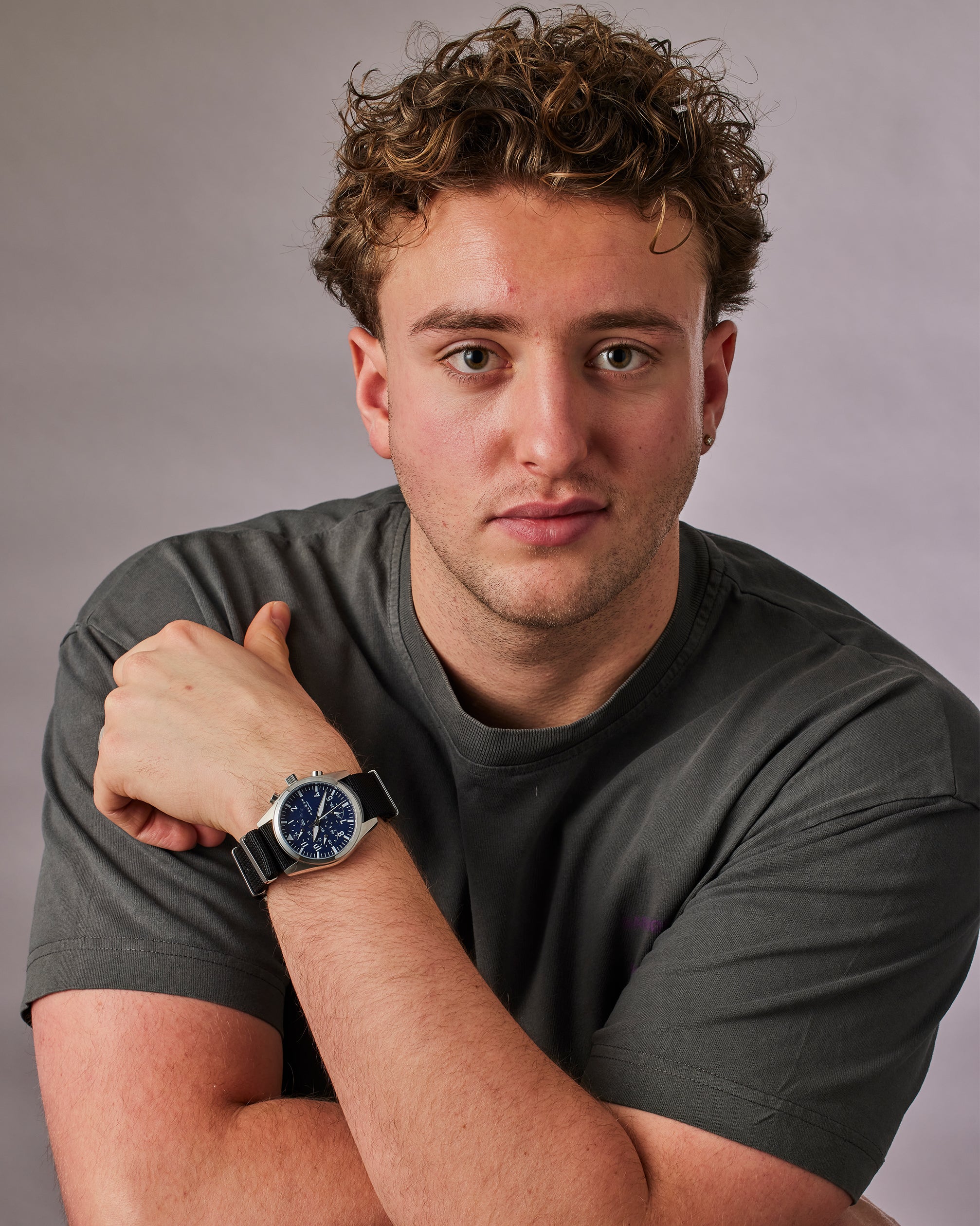 Man wearing a dark gray t-shirt and a watch with a blue face on a gray background