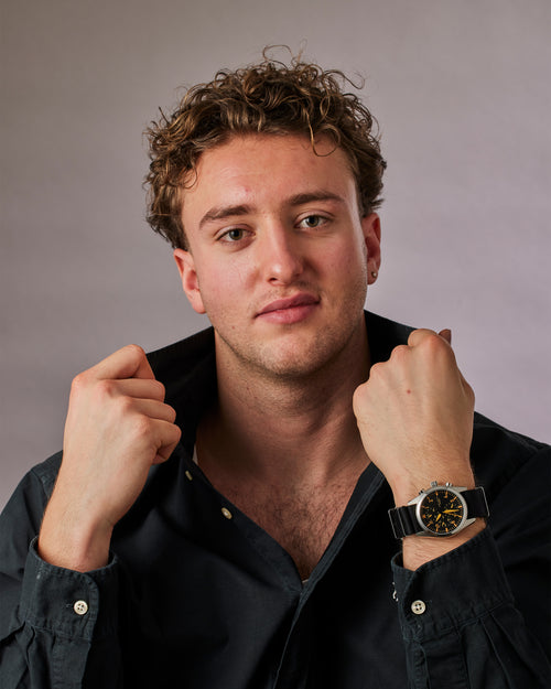 Man wearing a black shirt and a watch, posing against a plain background