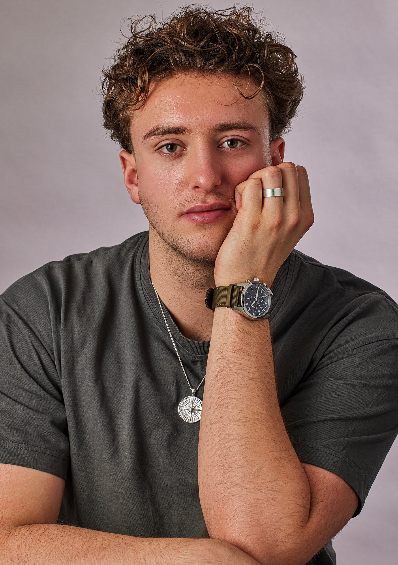 Man wearing a gray t-shirt and watch, resting his head on his hand against a plain background