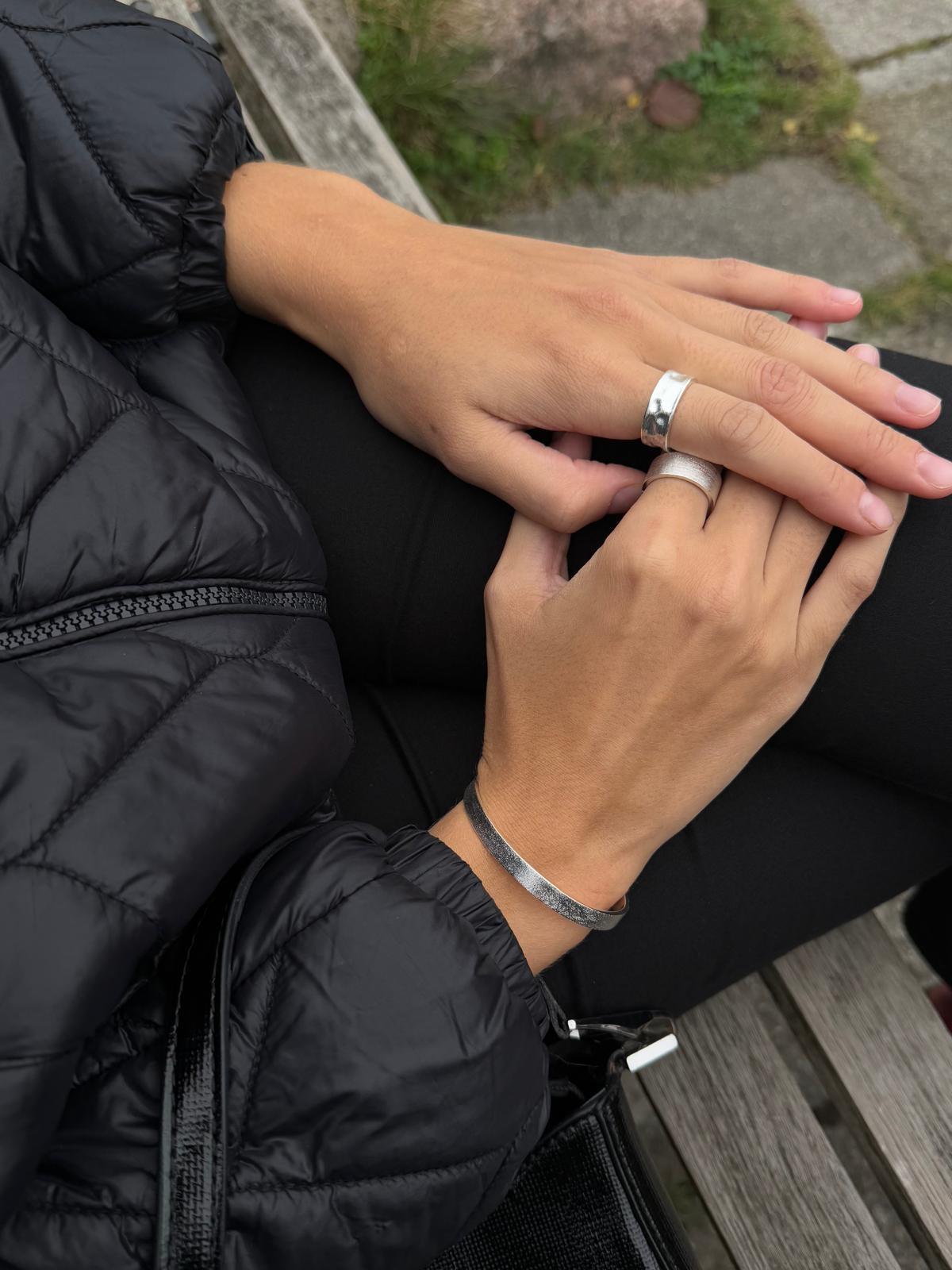 Person wearing two silver rings on their fingers, sitting outdoors.