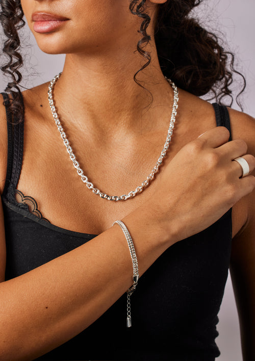 Woman wearing a silver necklace, bracelet, and ring on a neutral background